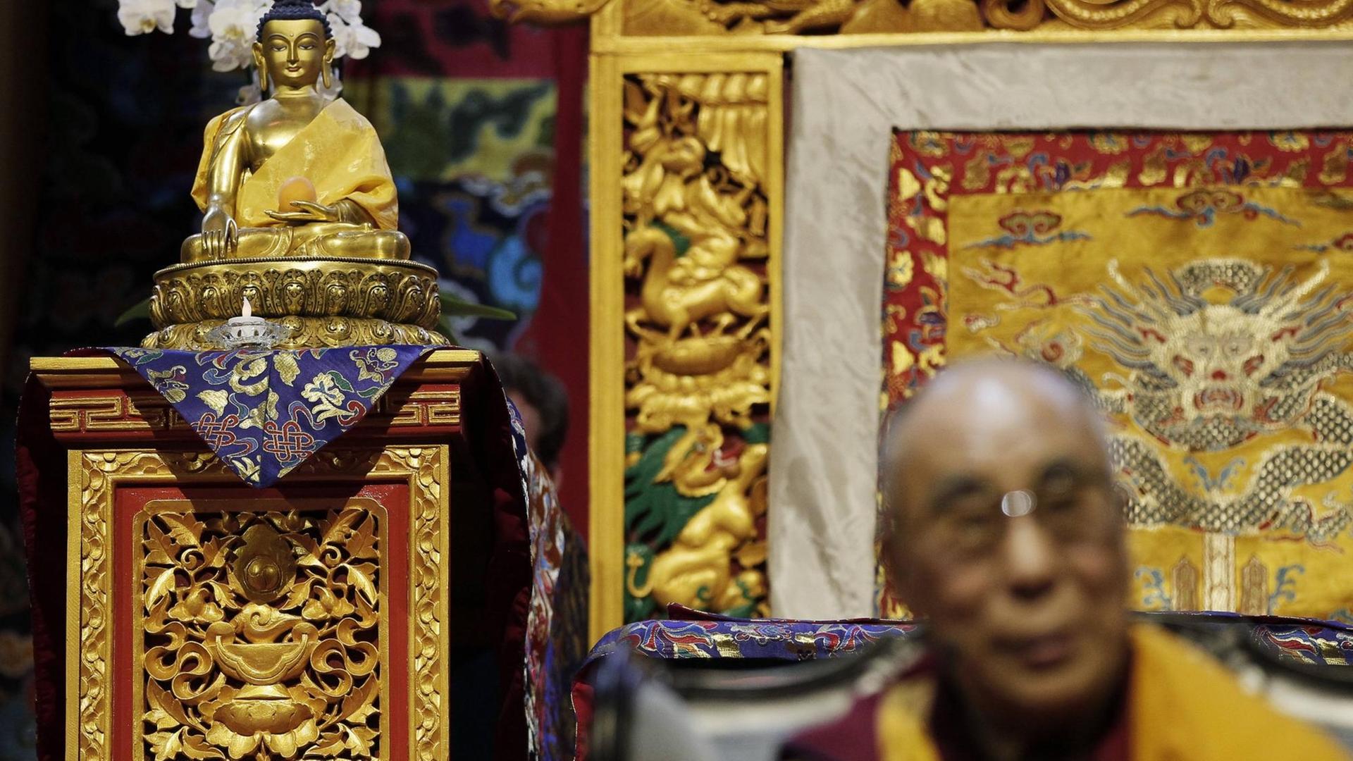 Der Dalai Lama unscharf im Vordergrund, neben einem Buddha. Der Dalai Lama unscharf im Vordergrund, neben einem Buddha.