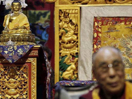 Der Dalai Lama unscharf im Vordergrund, neben einem Buddha.