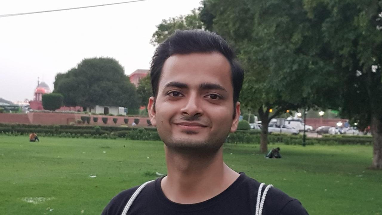 Ein junger Mann steht im T-Shirt auf einer Wiese. Im Hintergrund eine Ortschaft. Ein junger Mann steht im T-Shirt auf einer Wiese. Im Hintergrund eine Ortschaft.