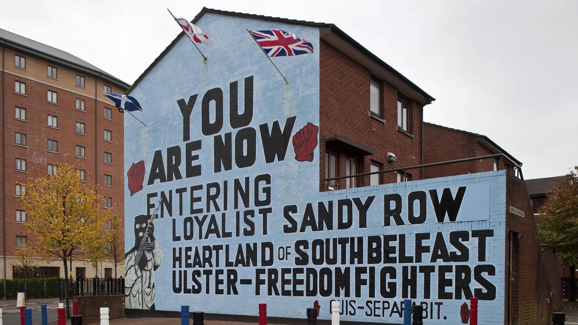 Bemalte Häuserfassade in Sandy Row, Belfast 2009: Links unten: ein maskierter und bewaffneter loyalistischer Kämpfer. Links und rechts oben: zwei geballte Fäuste, die für die Rote Hand von Ulster stehen und Symbol der UFF Bemalte Häuserfassade in Sandy Row, Belfast 2009: Links unten: ein maskierter und bewaffneter loyalistischer Kämpfer. Links und rechts oben: zwei geballte Fäuste, die für die Rote Hand von Ulster stehen und Symbol der UFF
