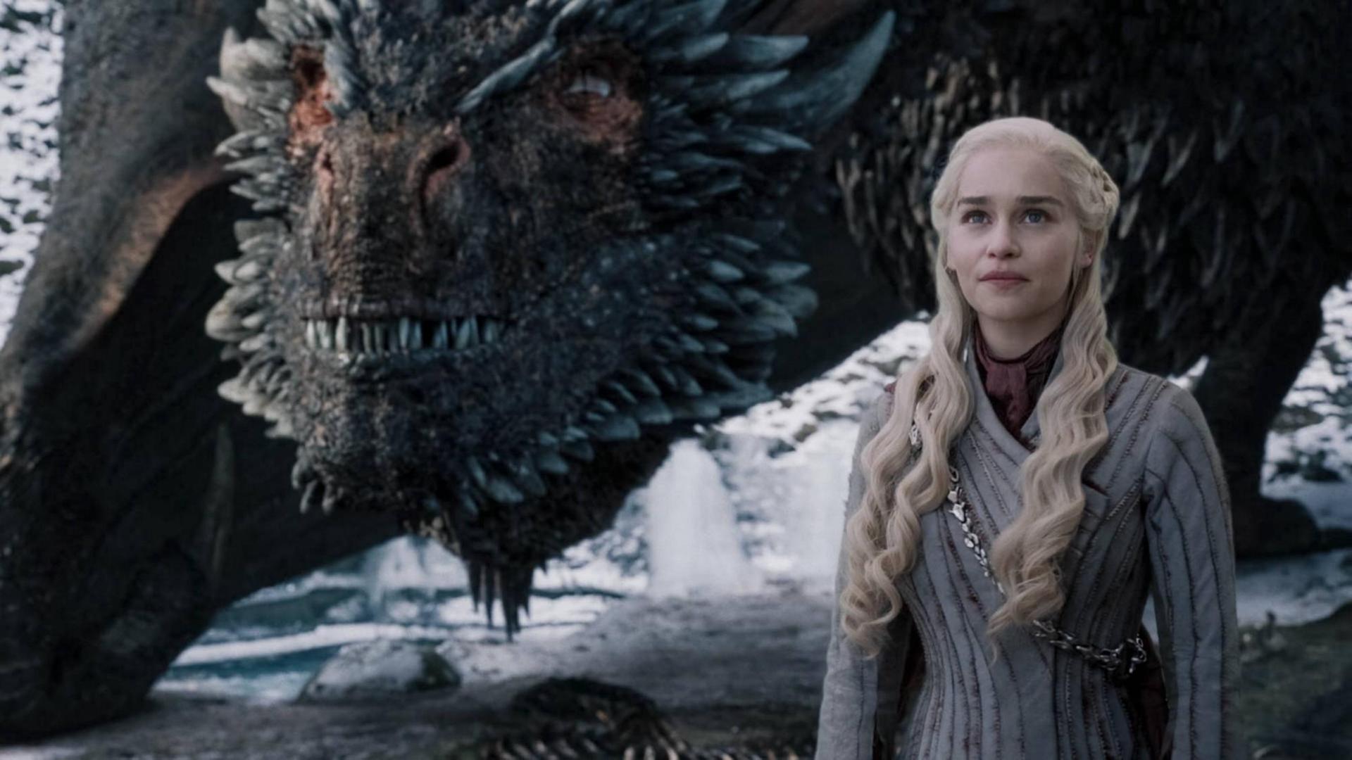 Im Vordergrund steht die Schauspielerin Emilia Clarke. Sie trägt einen Mantel und lange blonde gewellte Haare. Im Hintergrund ein riesiger Drache. Im Vordergrund steht die Schauspielerin Emilia Clarke. Sie trägt einen Mantel und lange blonde gewellte Haare. Im Hintergrund ein riesiger Drache.
