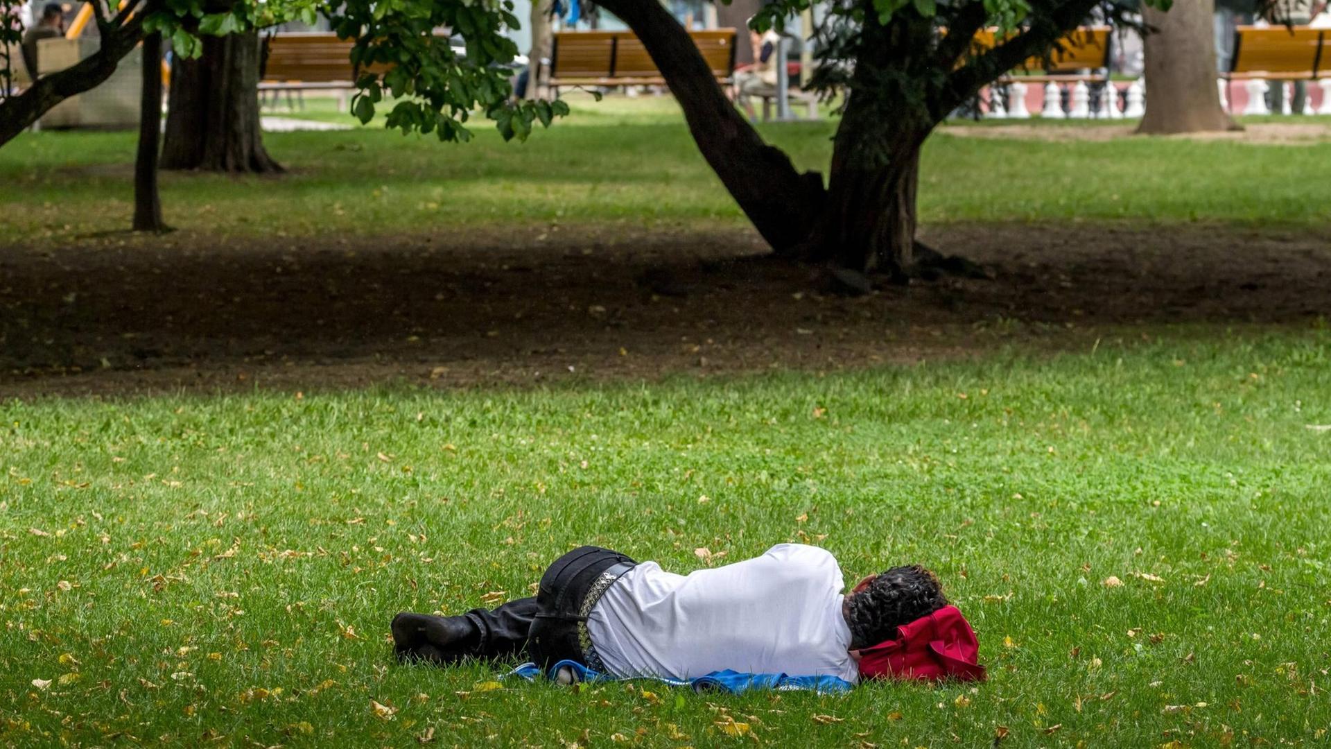 Mann in sommerlichem Business-Anzug schläft auf einer Wiese vor einem Gebäude Mann in sommerlichem Business-Anzug schläft auf einer Wiese vor einem Gebäude