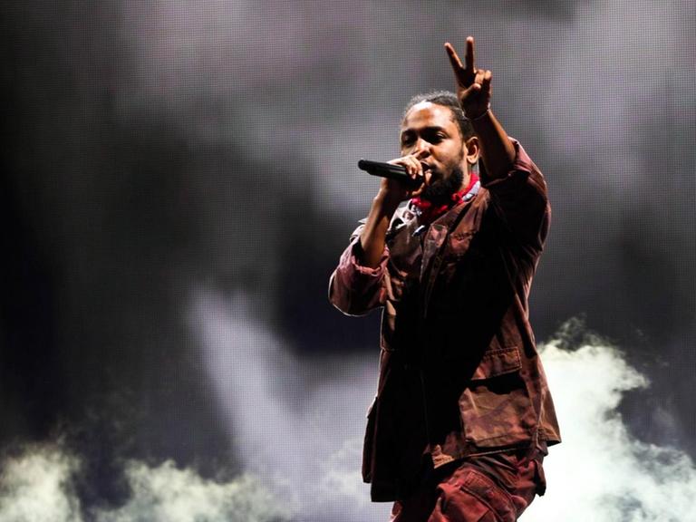 Kendrick Lamar beim Panorama Music Festival 2016 in New York. Der Musiker steht vor dunklem Hintergrund und macht mit einer Hand das Peace-Zeichen