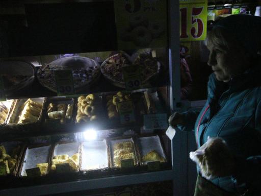 Eine Frau vor einem notdürftig beleuchteten Lebensmittelgeschäft