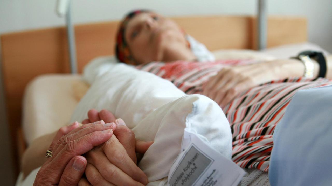 Eine ehrenamtliche Helferin hält die Hand einer sterbenden Bewohnerin, die in ihrem Bett im Christophorus Hospiz in München liegt Eine ehrenamtliche Helferin hält die Hand einer sterbenden Bewohnerin, die in ihrem Bett im Christophorus Hospiz in München liegt