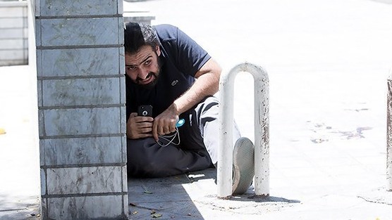 Der Mann kauert mit angstverzerrtem Gesicht hinter einer Mauer. Er hält ein Handy in der Hand. Der Mann kauert mit angstverzerrtem Gesicht hinter einer Mauer. Er hält ein Handy in der Hand.