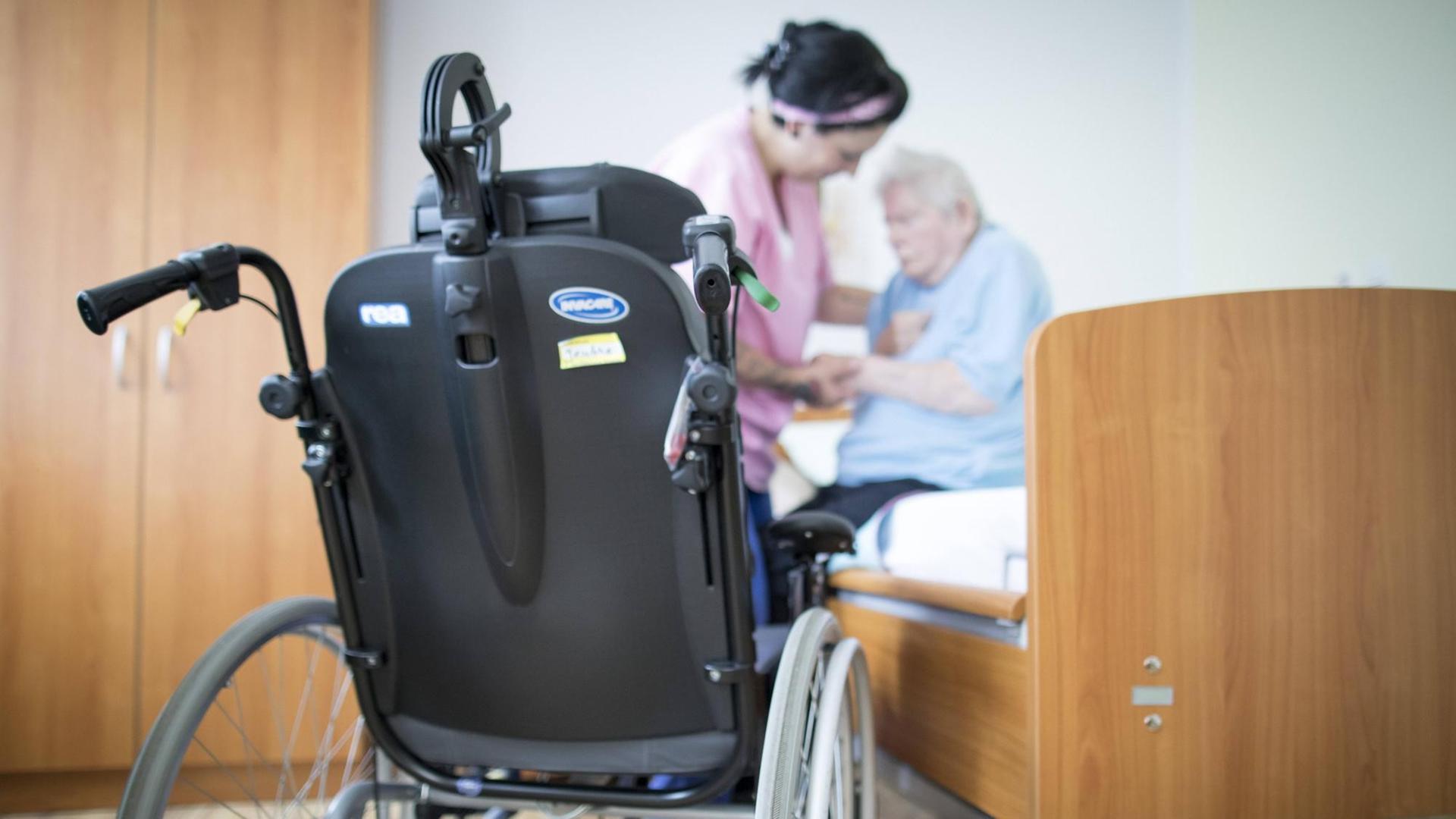 Eine Altenpflegerin hilft einer Bewohnerin in einem Altenpflegeheim aus dem Bett. Im Vordergrund steht ein Rollstuhl. Eine Altenpflegerin hilft einer Bewohnerin in einem Altenpflegeheim aus dem Bett. Im Vordergrund steht ein Rollstuhl.