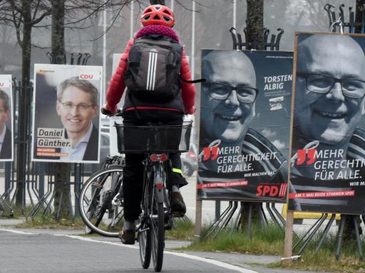 Ein Radfahrer fährt in Kiel an Wahlplakaten mit den Spitzenkandidaten der Landtagswahl, Daniel Günther (CDU) und Torsten Albig (SPD), vorbei