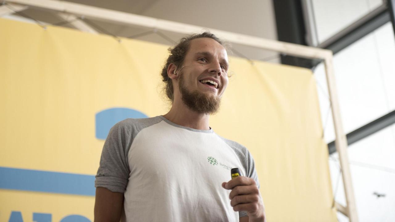Tobi Rosswog bei einer Konferenz an der Alanus Hochschule in NRW. Ein Mann mit langen Haaren und Bart spricht zu Menschen. Tobi Rosswog bei einer Konferenz an der Alanus Hochschule in NRW. Ein Mann mit langen Haaren und Bart spricht zu Menschen.