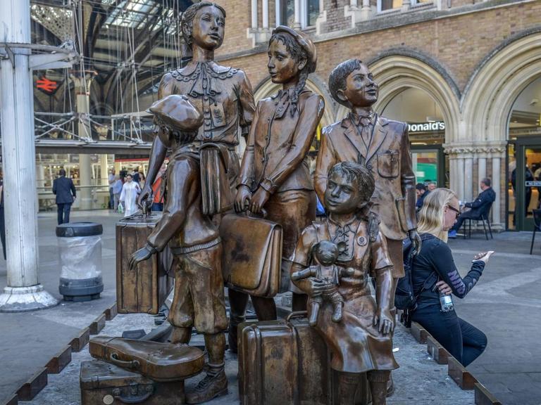 Das Foto zeigt das Denkmal "Kindertransport – Die Ankunft", Vorplatz der Liverpool Street Station, London. Das Denkmal stellt ankommende geflüchtete jüdische Kinder mit ihrem Gepäck dar.