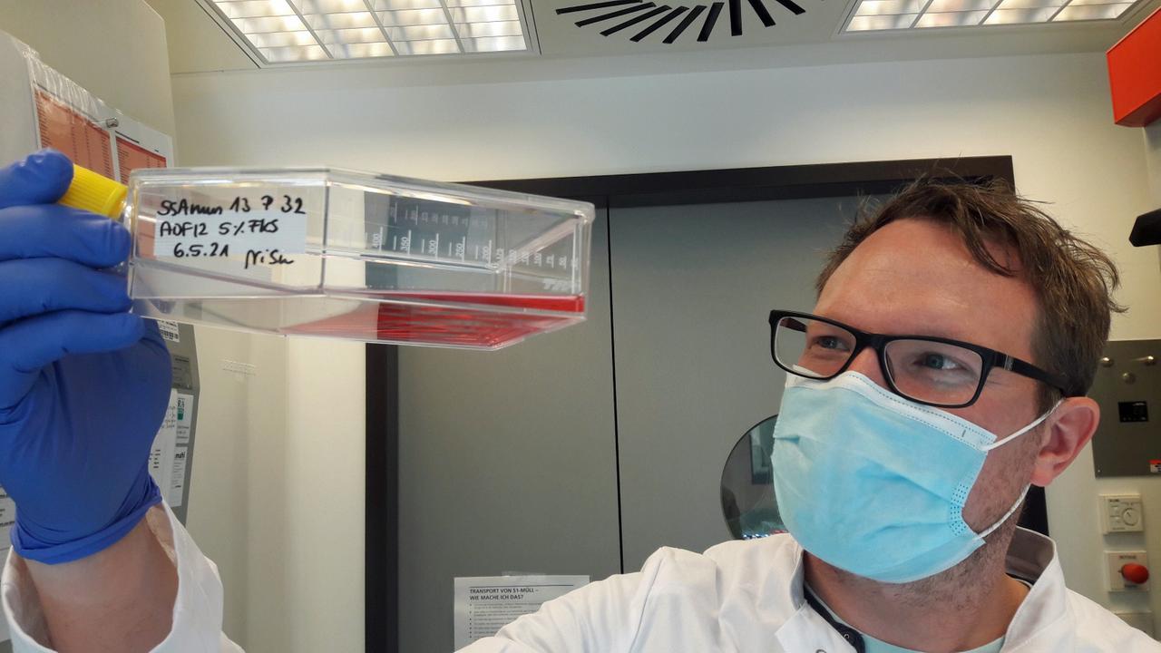 Sebastian Rakers hält einen durchsichtigen Behälter mit einer rötlichen Flüssigkeit nach oben. Sebastian Rakers hält einen durchsichtigen Behälter mit einer rötlichen Flüssigkeit nach oben.