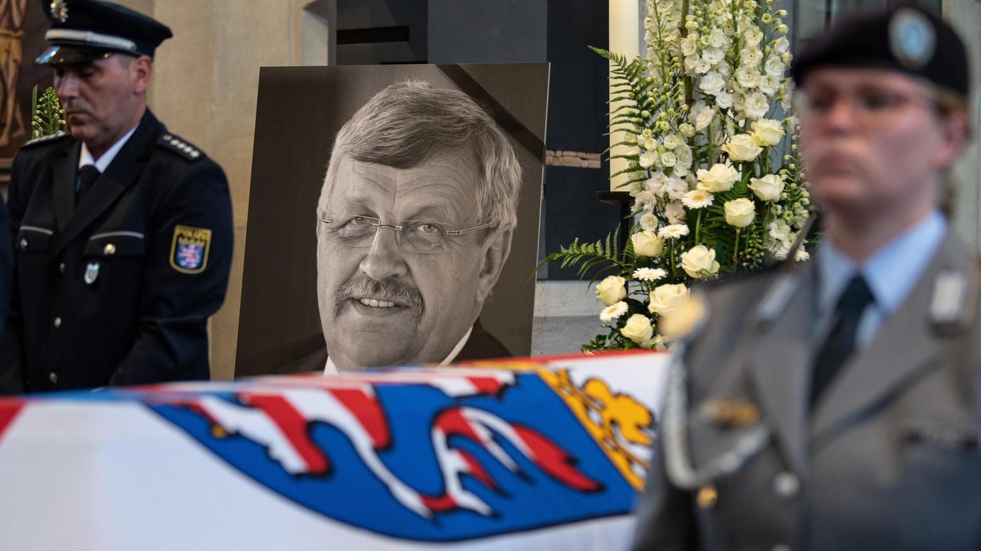 dpatopbilder - 13.06.2019, Hessen, Kassel: Das Konterfei von Walter Lübcke (CDU) ist hinter einem Bundeswehrsoldaten am Sarg bei einem Trauergottesdienst in der Martinskirche zu sehen. Lübcke wurde mit einem Kopfschuss auf der Terrasse seines Wohnhauses getötet. Foto: Swen Pförtner/dpa-POOL/dpa | Verwendung weltweit
