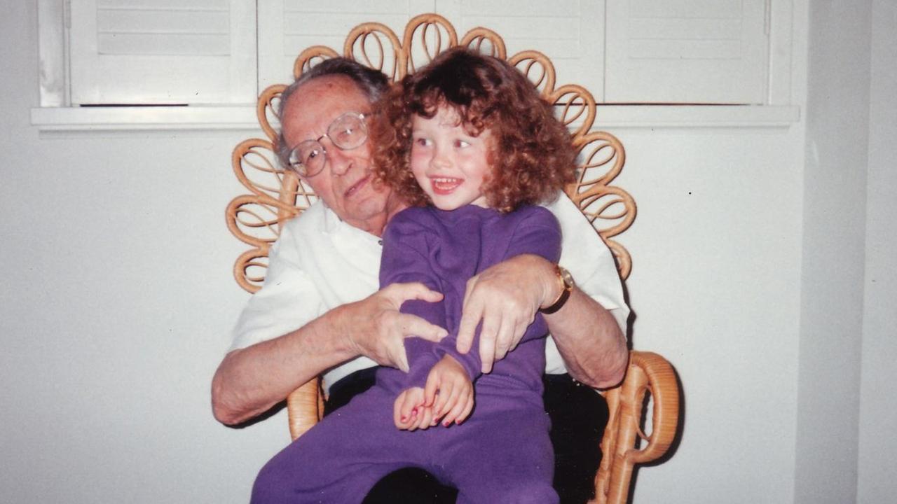 Ein alter Mann sitzt auf einem Korbstuhl, auf seinem Schoß sitzt seine rotgelockte Enkelin