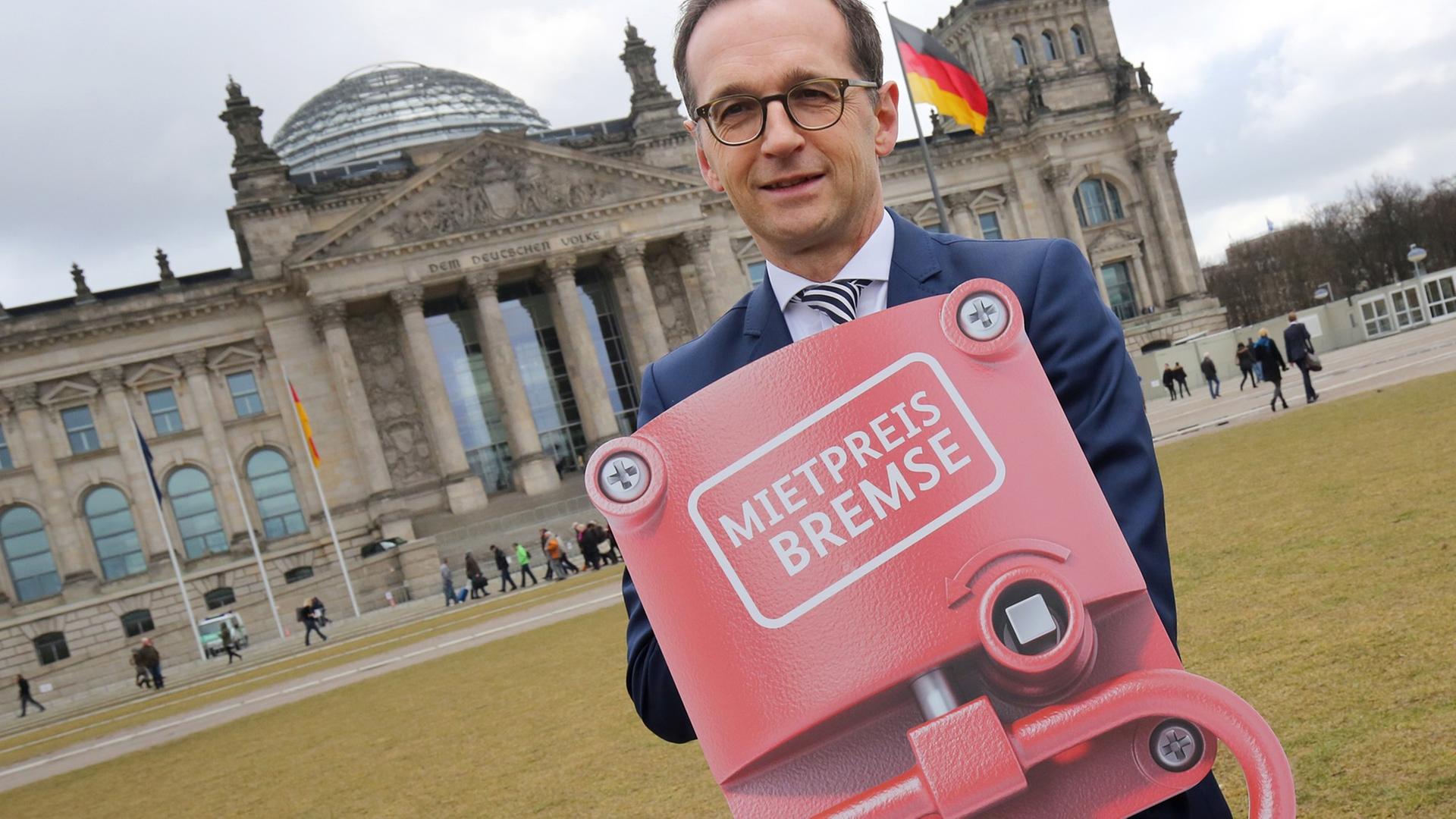 Heiko Maas steht auf der Wiese vor dem Reichstag und hält ein Schild in Händen, das eine Notbremse darstellt und auf dem "Mietpreisbremse" steht. Heiko Maas steht auf der Wiese vor dem Reichstag und hält ein Schild in Händen, das eine Notbremse darstellt und auf dem "Mietpreisbremse" steht.