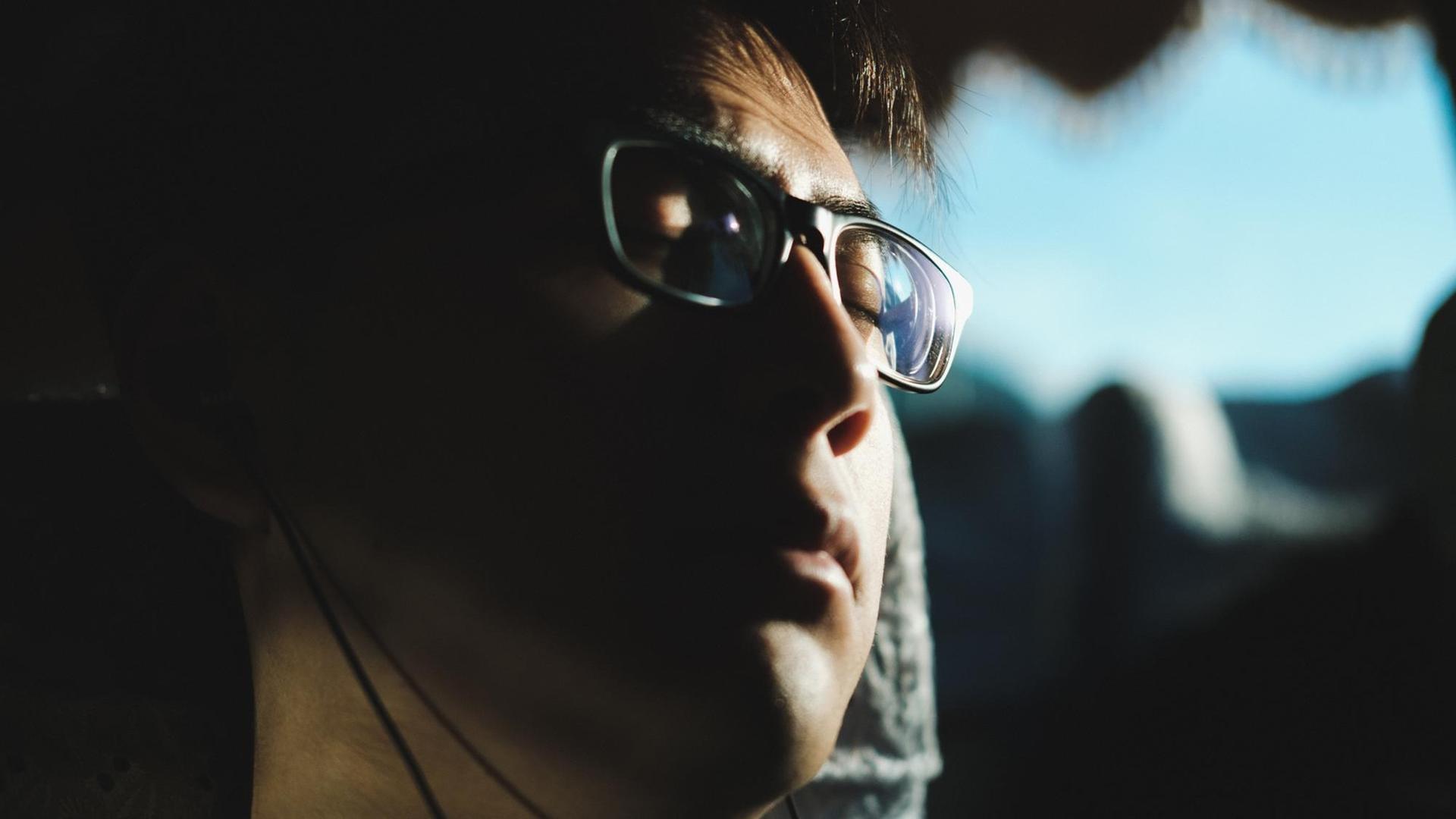 Das Bild zeigt einen Mann mit Kopfhörern im Gegenlicht. Seine Augen sind geschlossen, er trägt In-Ear-Kopfhörer. Das Bild zeigt einen Mann mit Kopfhörern im Gegenlicht. Seine Augen sind geschlossen, er trägt In-Ear-Kopfhörer.