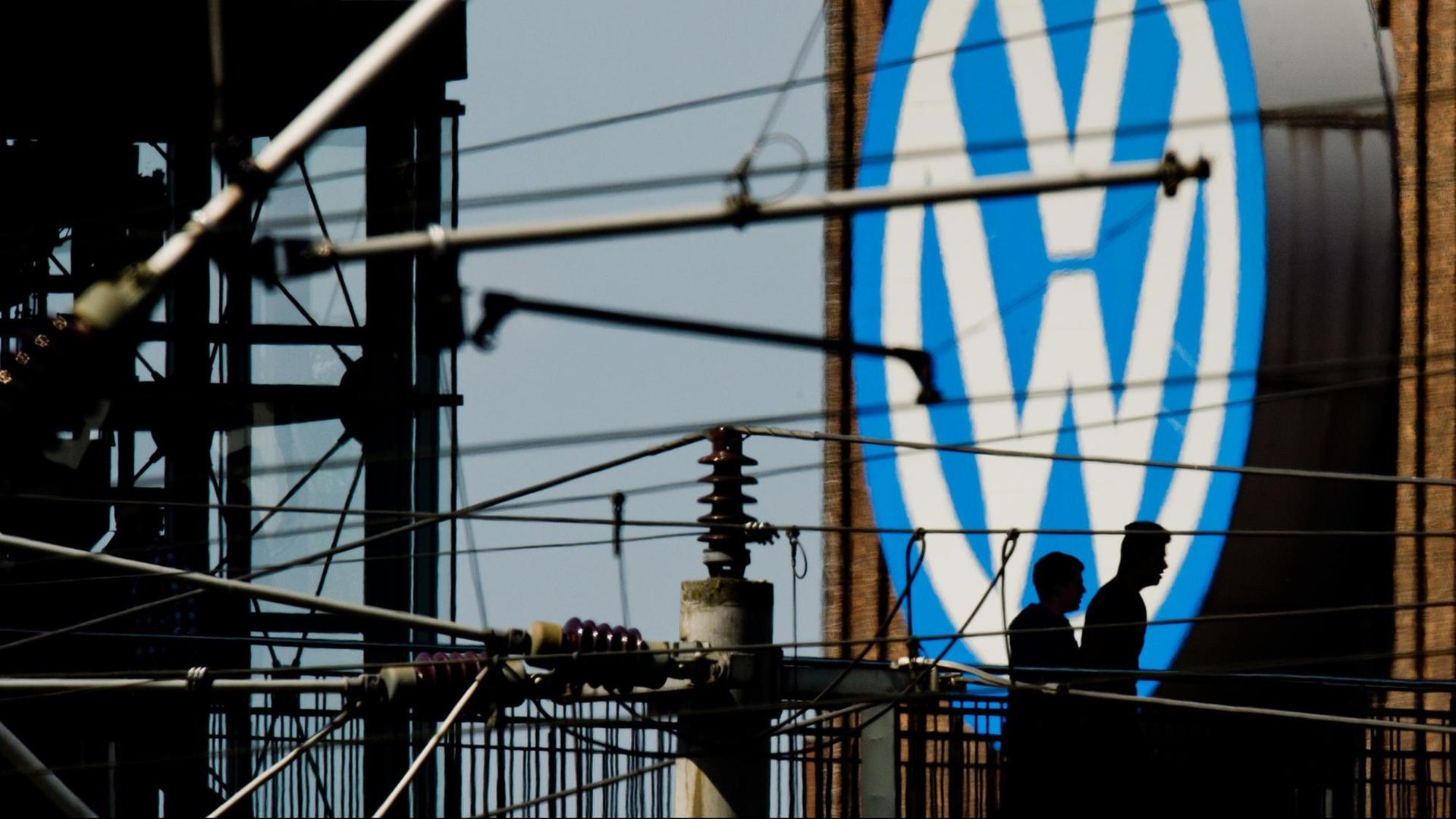 Die Silhouetten von zwei Männern auf einer Brücke zeichnen sich am 10.05.2016 vor dem großen Volkswagen-Logo am Kraftwerk am VW-Werk in Wolfsburg (Niedersachsen) ab. Die Silhouetten von zwei Männern auf einer Brücke zeichnen sich am 10.05.2016 vor dem großen Volkswagen-Logo am Kraftwerk am VW-Werk in Wolfsburg (Niedersachsen) ab.