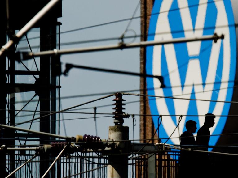 Die Silhouetten von zwei Männern auf einer Brücke zeichnen sich am 10.05.2016 vor dem großen Volkswagen-Logo am Kraftwerk am VW-Werk in Wolfsburg (Niedersachsen) ab.