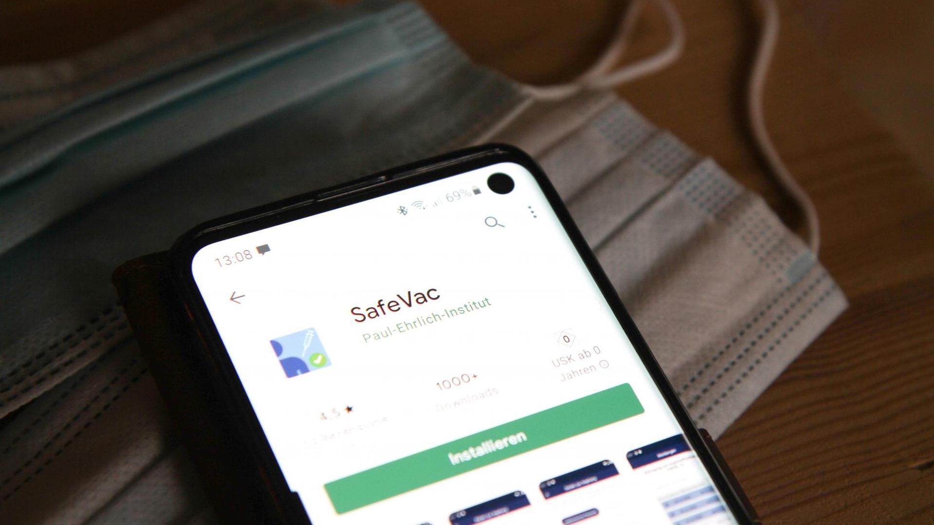 Ein Smartphone mit der App SafeVac liegt auf blauen Einwegschutzmasken. Ein Smartphone mit der App SafeVac liegt auf blauen Einwegschutzmasken.