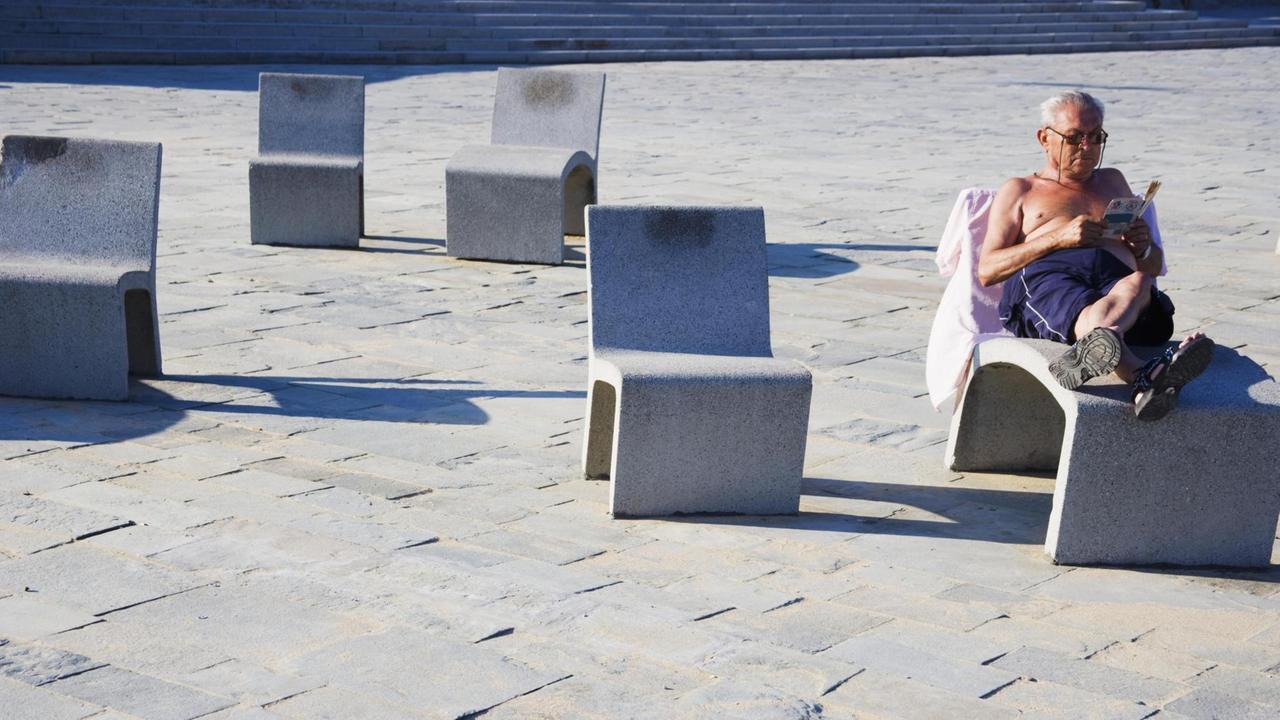 Älterer Herr bei einer Ruhepause auf einem Betonsessel an der Strandpromenade von Barcelona Älterer Herr bei einer Ruhepause auf einem Betonsessel an der Strandpromenade von Barcelona