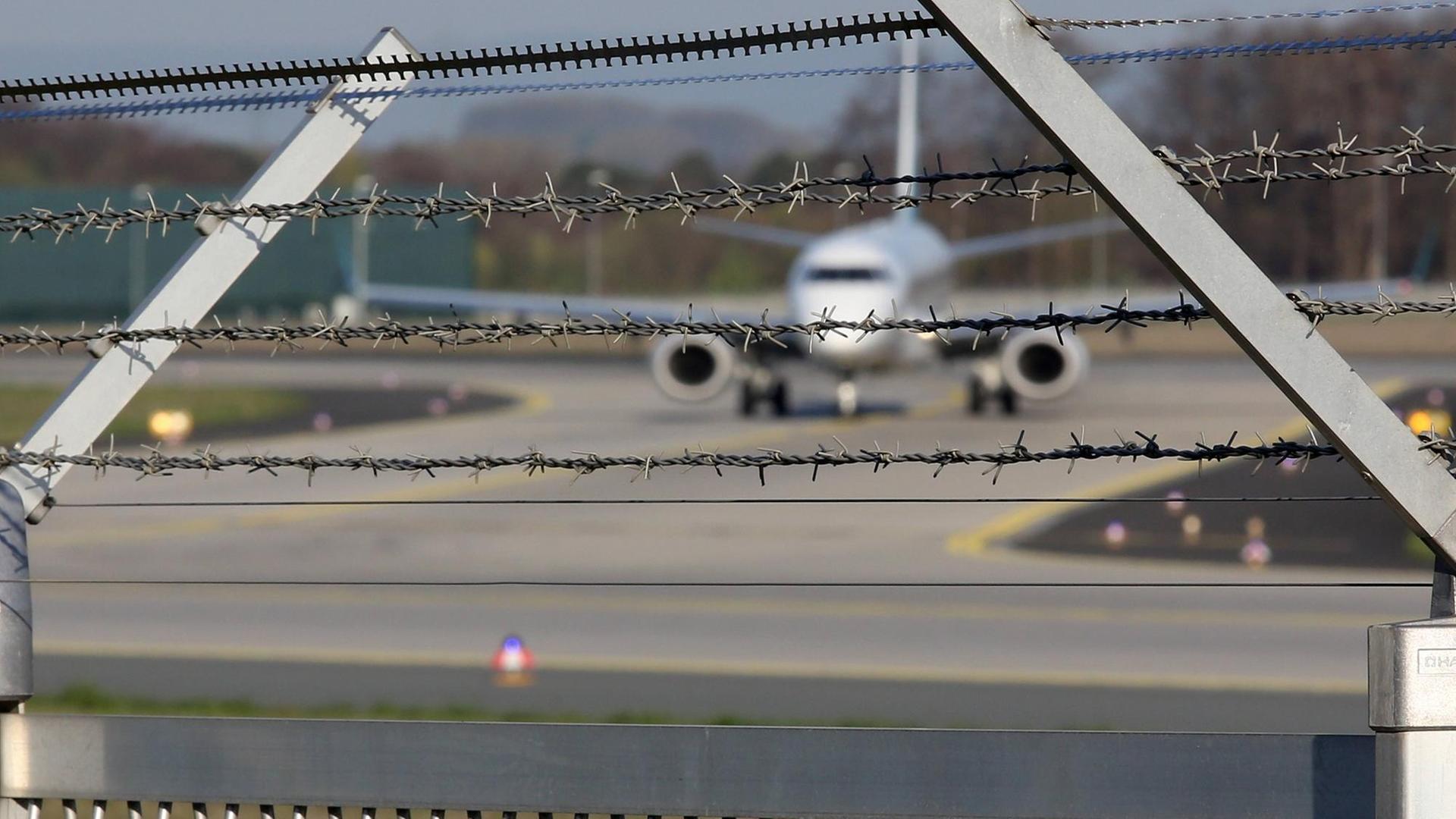 Symbolfoto zum Thema Abschiebung: Im Vordergrund ist ein Zaun mit Sacheldraht zu sehen, im Hintergrund ein Flugzeug auf dem Flughafen Frankfurt am Main.
