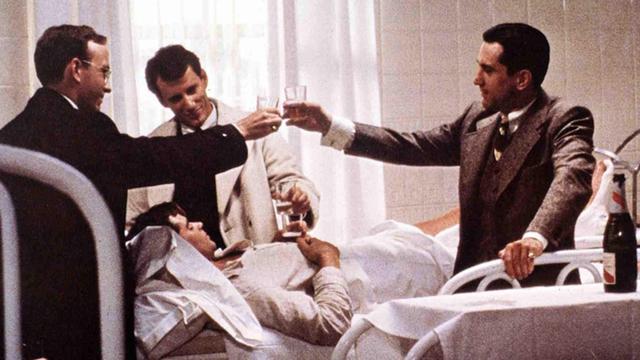 Szene aus dem Film "Es war einmal in Amerika" von 1984 mit den SchauspielernTreat Williams (liegend ), James Woods, Robert De Niro in der Regie von Sergio Leone. Am Krankenbett wird mit Alkohol angestoßen.
