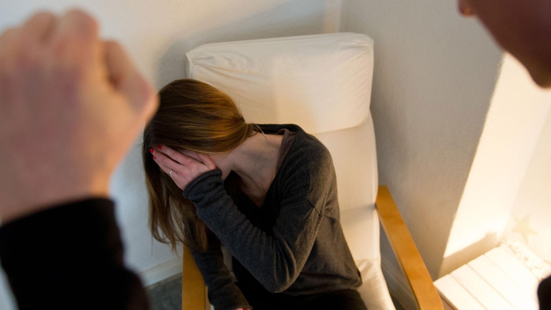 Ein Mann ballt seine Hand zur Faust, vor ihm eine Frau auf einem Sessel, die sich ängstlich die Hand vor ihr Gesicht hält. Ein Mann ballt seine Hand zur Faust, vor ihm eine Frau auf einem Sessel, die sich ängstlich die Hand vor ihr Gesicht hält.