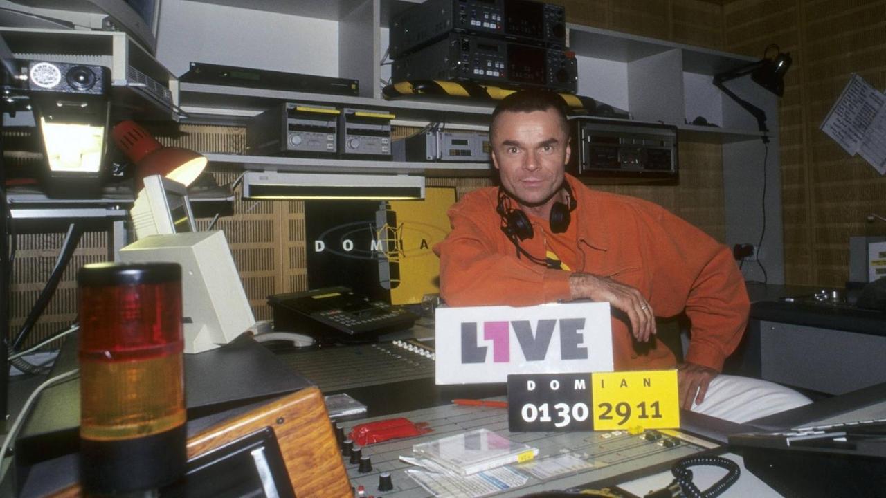 Jürgen Domian sitzt 1996 im 1Live-Studio, von dem erseine Sendung "Domian" moderierte - im Vordergrund ein Schild mit der Telefonnummer für die Hörerinnen und Hörer Jürgen Domian sitzt 1996 im 1Live-Studio, von dem erseine Sendung "Domian" moderierte - im Vordergrund ein Schild mit der Telefonnummer für die Hörerinnen und Hörer