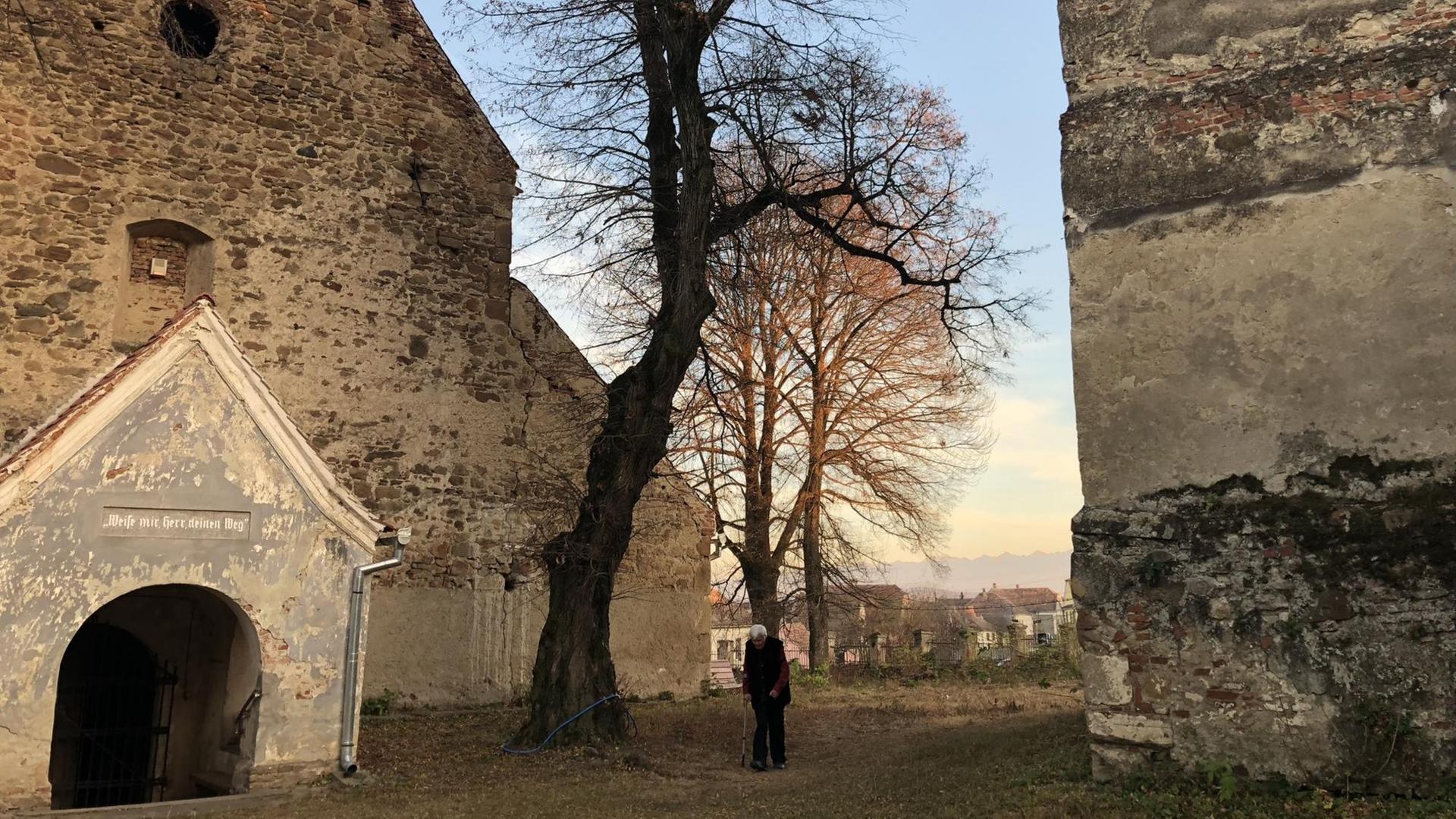 Eginald Schlattner geht auf einen Stock gestützt an einer alten Kirche entlang Eginald Schlattner geht auf einen Stock gestützt an einer alten Kirche entlang