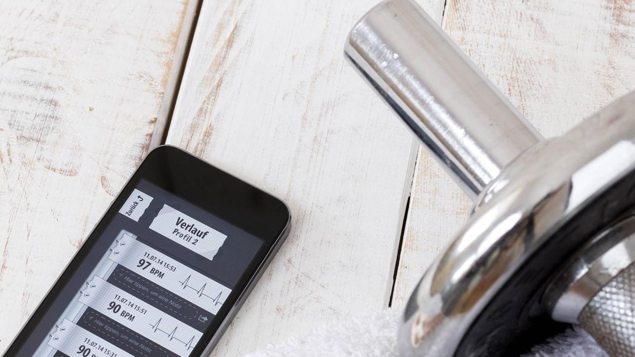 Smartphone mit einer Fitness-App, daneben eine Hantel auf einem Handtuch Smartphone mit einer Fitness-App, daneben eine Hantel auf einem Handtuch