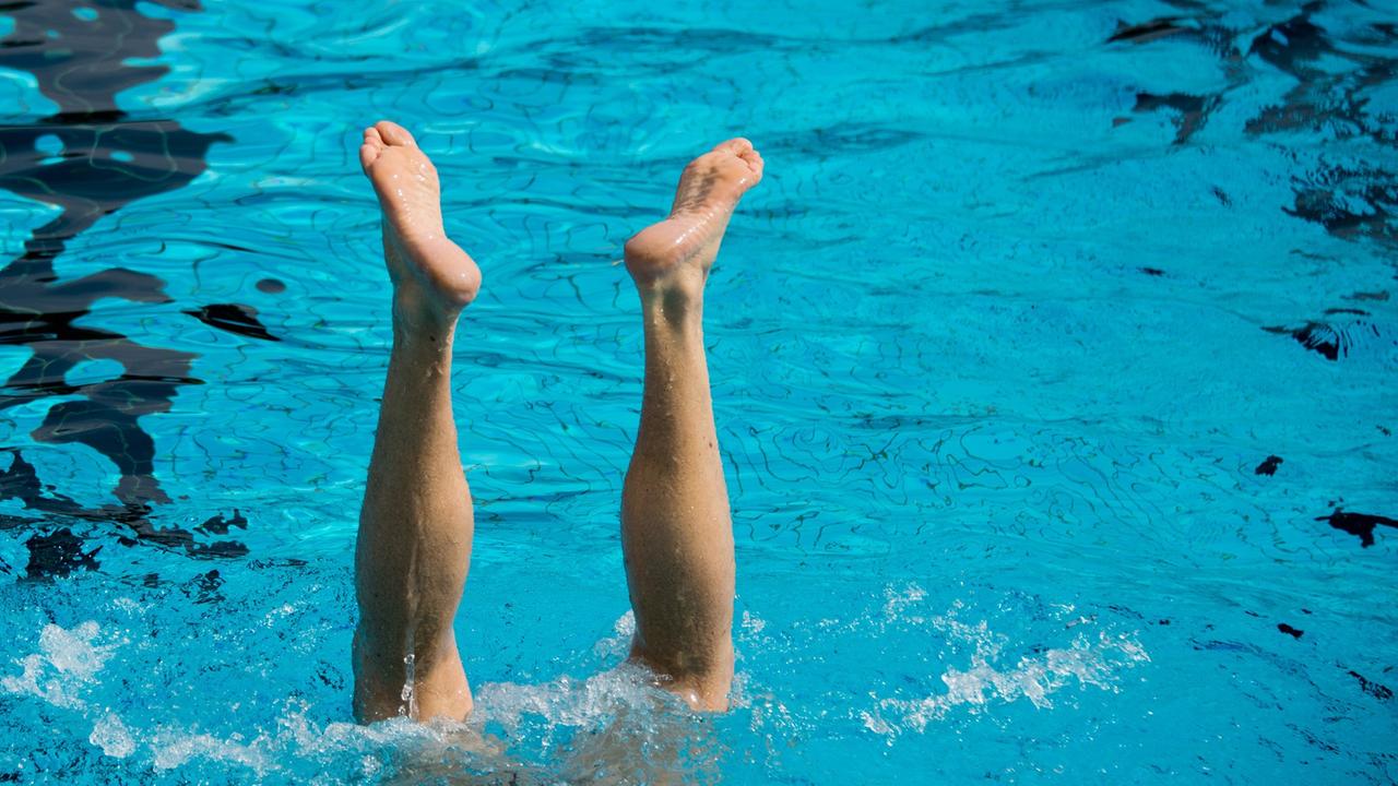 Ein Mann macht einen Handstand im Schwimmbecken eines Freibades. 