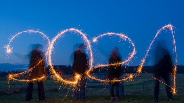 Vier Personen stehen auf einem Feld und schreiben mit Wunderkerzen die Jahreszahl "2021" in den Abendhimmel (Langzeitbelichtung, gestellte Aufnahme).