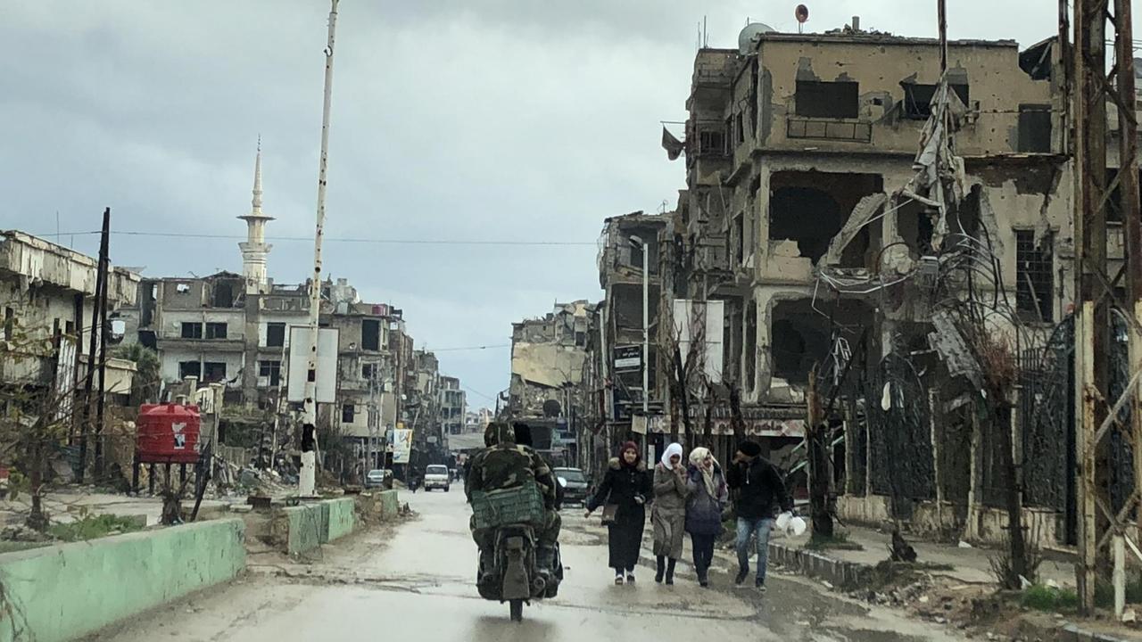 In der syrischen Stadt Dum laufen Mädchen auf einer Straße mit zerstörten Gebäuden.