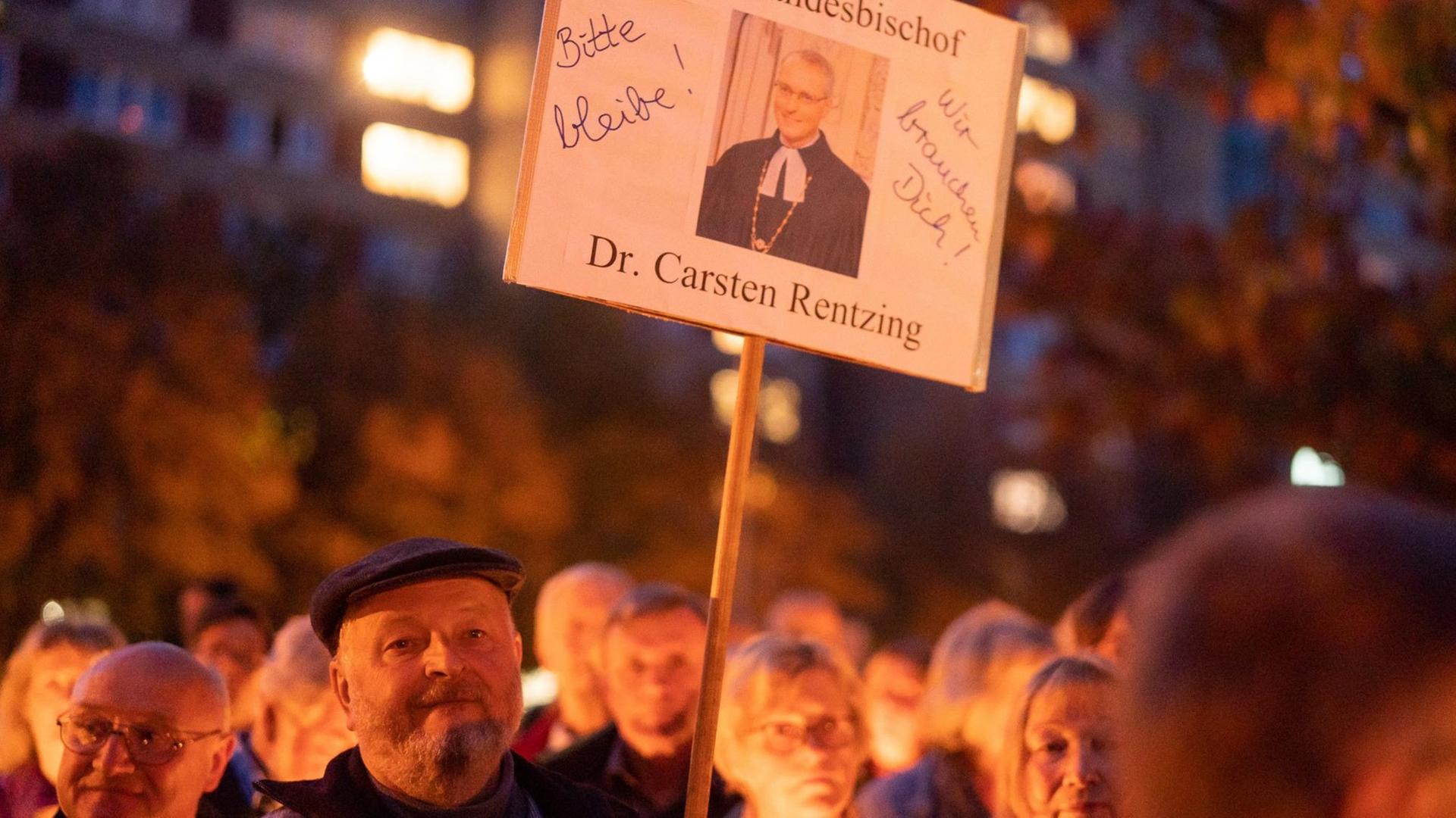 Ein Demonstrierender hält ein Schild mit einem Porträt von Carsten Rentzing und der Aufschrift "Bitte bleibe!"