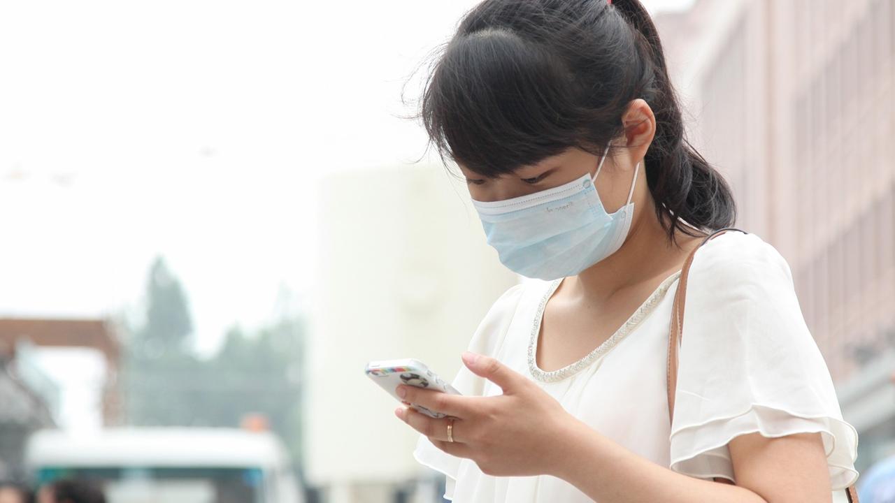 Eine Frau mit Smartphone (Handy) in der Hand traegt am 04.07.2014 einen Mundschutz im chinesischen Peking.
