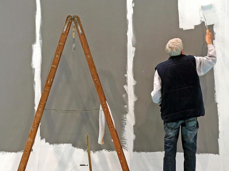 Ein älterer Mann streicht eine Wand.