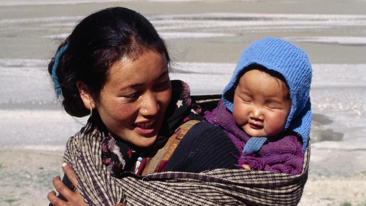 Eine Mutter aus dem Spiti-Tal in Himachal Pradesh, Indien, trägt ihr Kind in einem Tragetuch auf dem Rücken. 