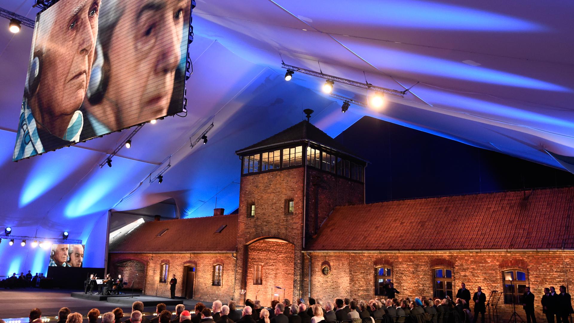 Bei der Gedenkveranstaltung vor dem Eingang des Konzentrationslagers Auschwitz ist ein Überlebender des Holocaust auf einer großen Leinwand zu sehen. Bei der Gedenkveranstaltung vor dem Eingang des Konzentrationslagers Auschwitz ist ein Überlebender des Holocaust auf einer großen Leinwand zu sehen.