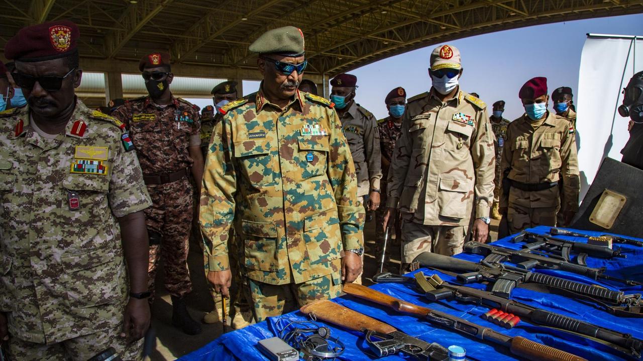 Männer in Uniformen stehen vor einem Tisch mit Waffen