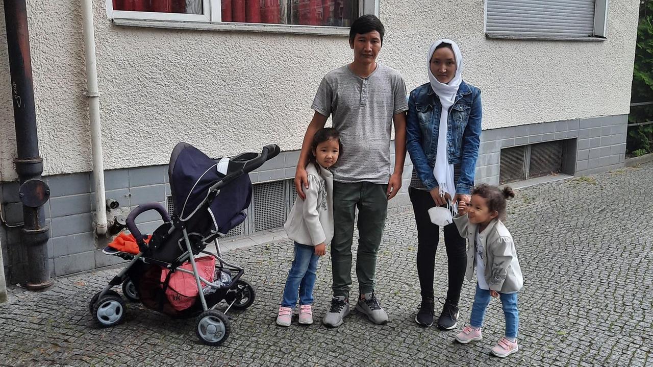Ein junge Mann und eine junge Frau stehen auf der Straße vor einem Neubau. Jeder der beiden hat ein kleines Mädchen an der Hand. Ein junge Mann und eine junge Frau stehen auf der Straße vor einem Neubau. Jeder der beiden hat ein kleines Mädchen an der Hand.