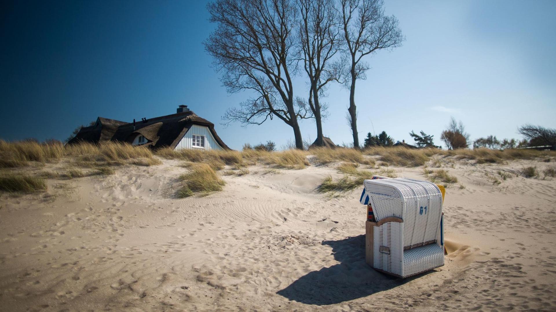 Ein Strandkorb am Strand von Ahrenshoop,vor einem Haus mit Reetdach und malerischer Strandkulisse. Ein Strandkorb am Strand von Ahrenshoop,vor einem Haus mit Reetdach und malerischer Strandkulisse.
