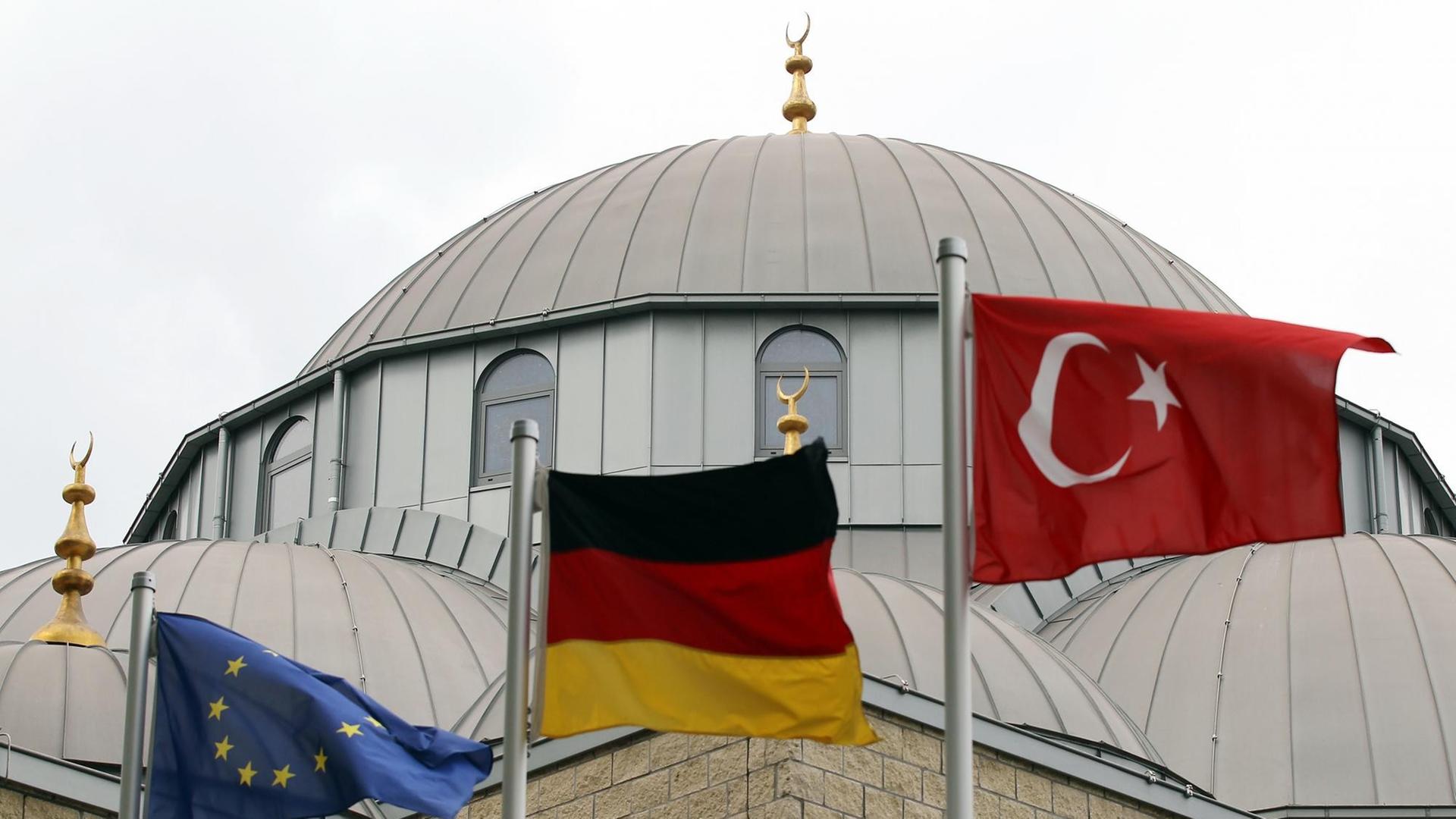 Eine europäische, eine deutsche und eine türkische Fahne (l-r) wehen am Freitag (10.09.2010) vor der Merkez-Moschee in Duisburg vor dem Beginn des Freitagsgebets. Die Debatte um die geplante Koran-Verbrennung in Florida hat die Feiertagsruhe der Muslime zum Ende des Ramadans gestört.