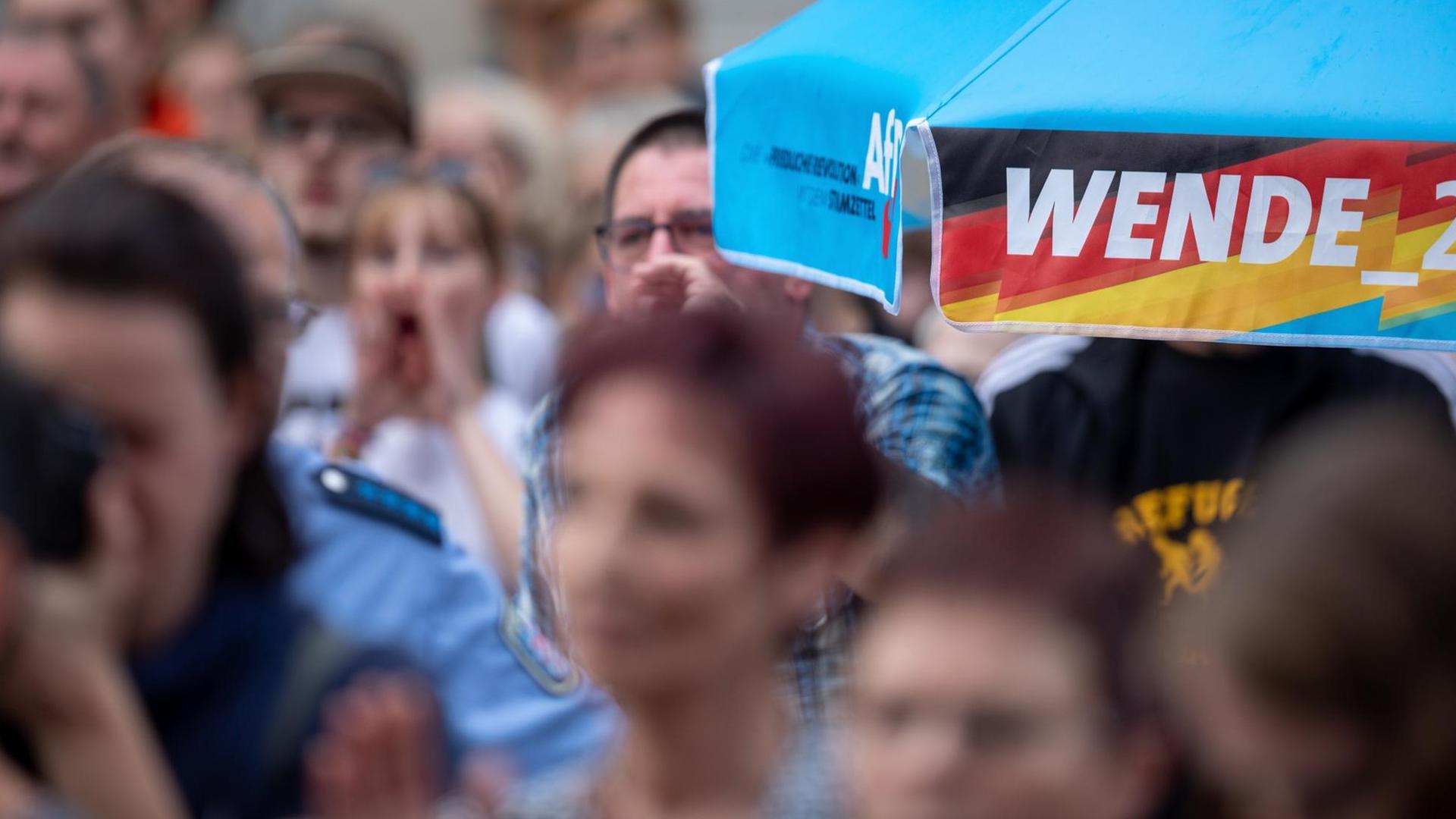 Protestierende auf einer Wahlkampfveranstaltung der AfD, rechts ein blauer Schirmrand, auf dem steht "Wende 2.0" Protestierende auf einer Wahlkampfveranstaltung der AfD, rechts ein blauer Schirmrand, auf dem steht "Wende 2.0"