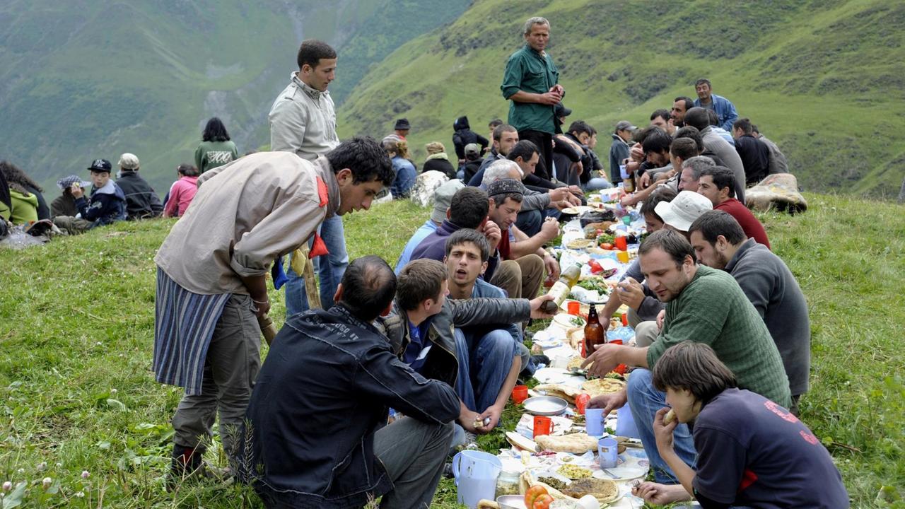 Männer beim Essen, Madoloba Fest auf dem Festplatz, Girevi, Tuschetien, Georgien. Männer beim Essen, Madoloba Fest auf dem Festplatz, Girevi, Tuschetien, Georgien.