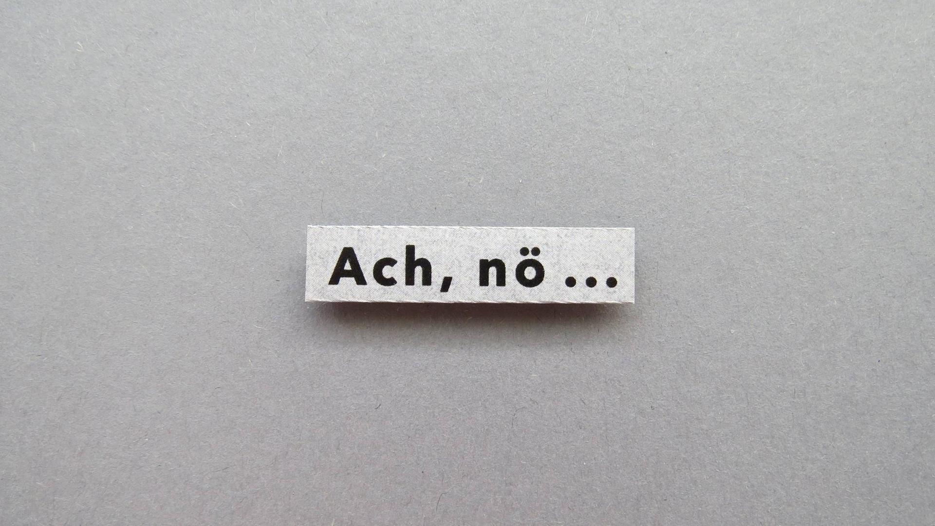 Auf einer ausgeschnittenen grauen Pappe steht "Ach. nö..." Auf einer ausgeschnittenen grauen Pappe steht "Ach. nö..."