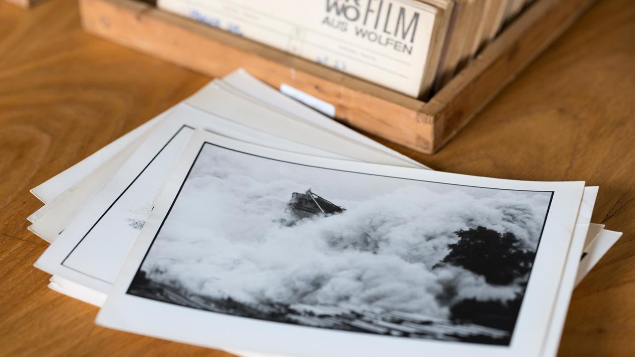 Auf einem Holztisch liegen ein Stapel Schwarz-Weiß-Fotos, im Hintergrund ein Zettelkasten voller Negative oder Fotos. Das oberste Foto zeigt einen Fels in der Brandung. Auf einem Holztisch liegen ein Stapel Schwarz-Weiß-Fotos, im Hintergrund ein Zettelkasten voller Negative oder Fotos. Das oberste Foto zeigt einen Fels in der Brandung.
