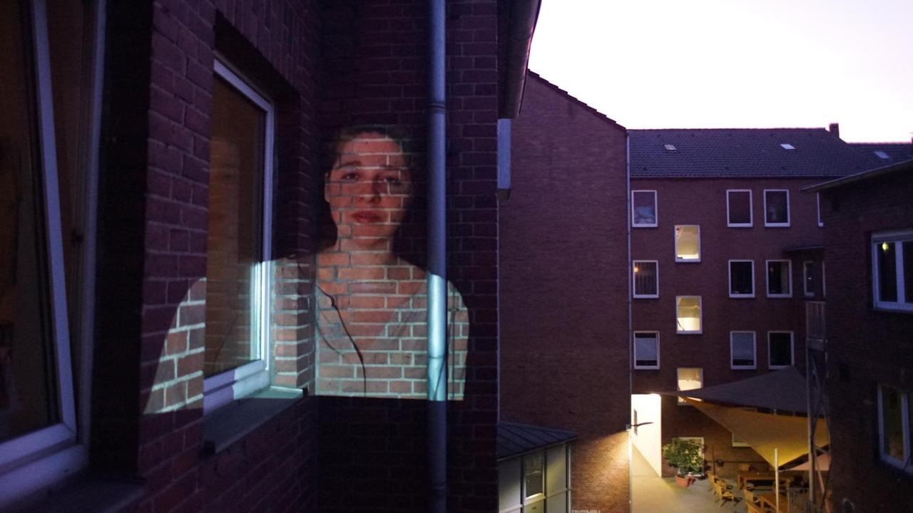 Eine Frau wird auf eine Häuserwand projiziert. Eine Frau wird auf eine Häuserwand projiziert.