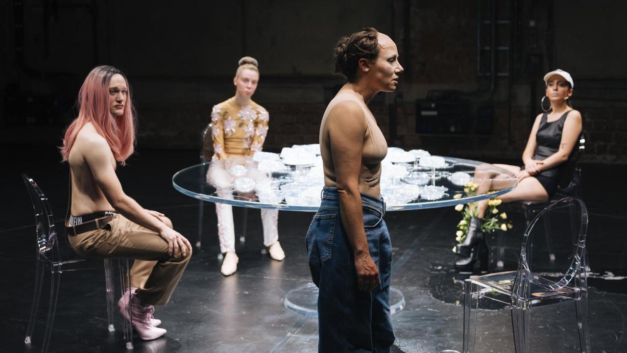 Szenenfoto der Theateraufführung "WUNDE R" in den Münchner Kammerspielen: Drei Menschen sitzen um einen Glastisch und schauen auf eine vierte Person, die davor steht. Auf der Bühne v.l.n.r. die Schauspieler Vincent Redetzki, Julia Windischbauer, Eva Löbau, Zeynep Bozbay Szenenfoto der Theateraufführung "WUNDE R" in den Münchner Kammerspielen: Drei Menschen sitzen um einen Glastisch und schauen auf eine vierte Person, die davor steht. Auf der Bühne v.l.n.r. die Schauspieler Vincent Redetzki, Julia Windischbauer, Eva Löbau, Zeynep Bozbay