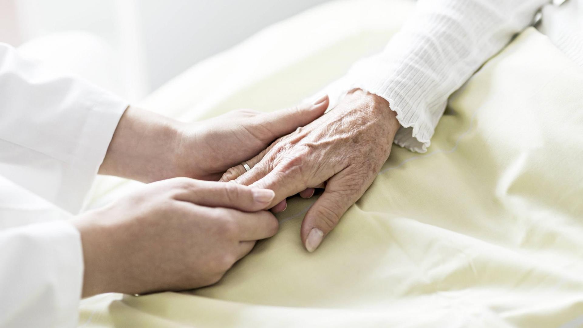Pflegerin hält die Hand einer Seniorin.