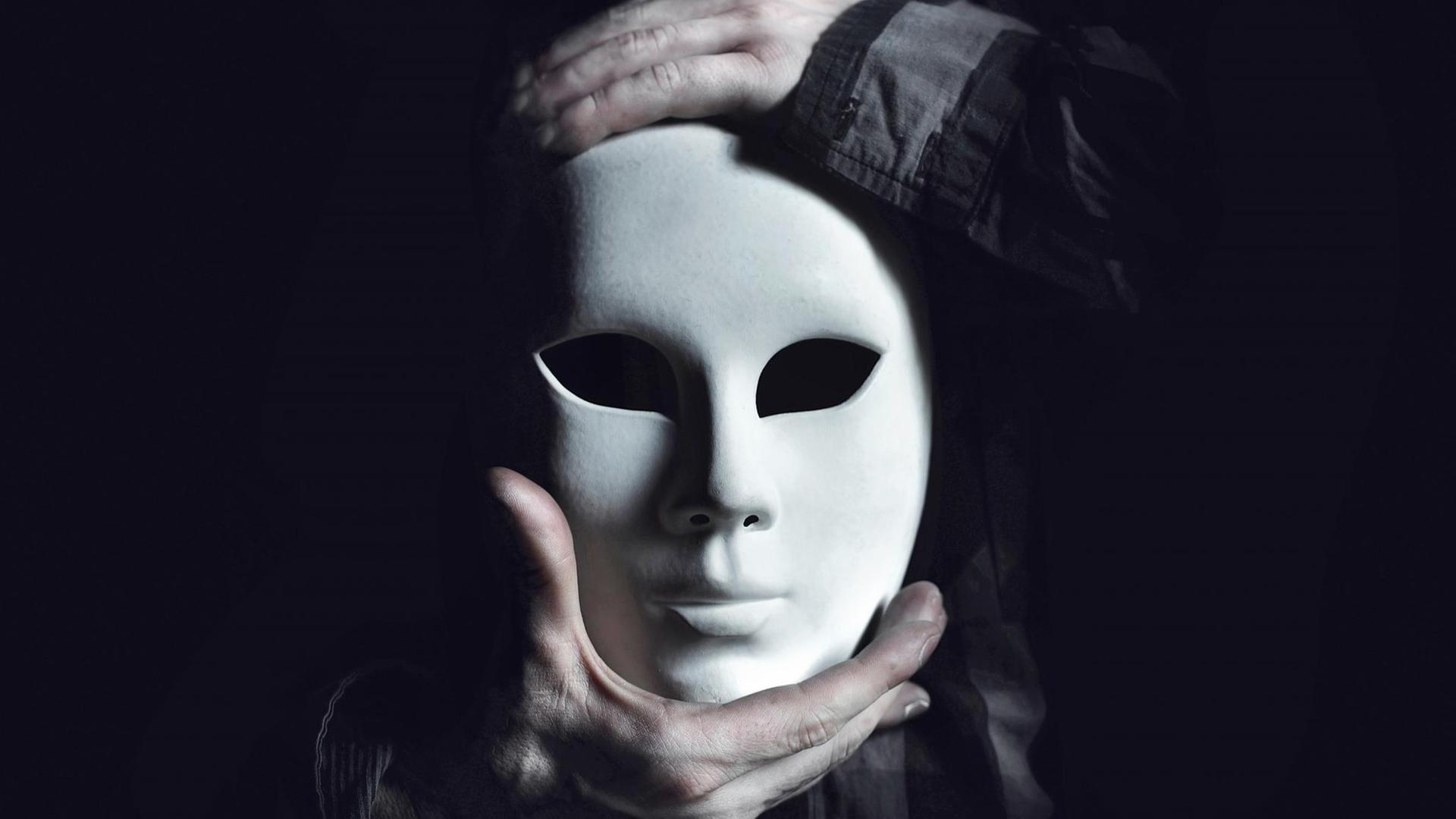 Die Hände eines Mannes halten eine weisse Maske. Die Hände eines Mannes halten eine weisse Maske.