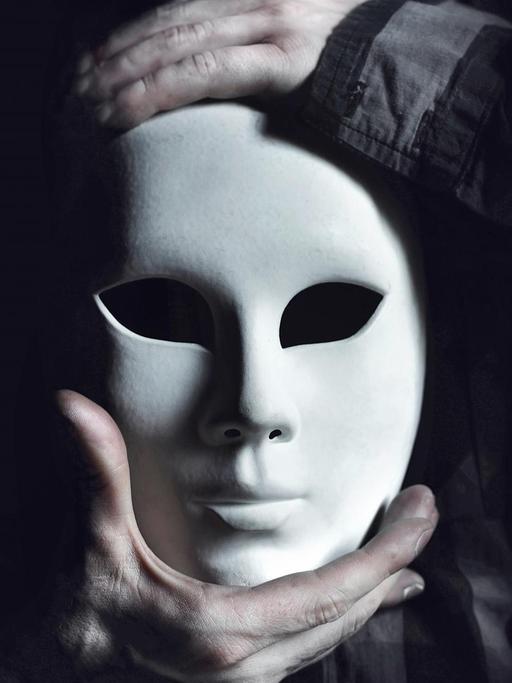 Die Hände eines Mannes halten eine weisse Maske.
